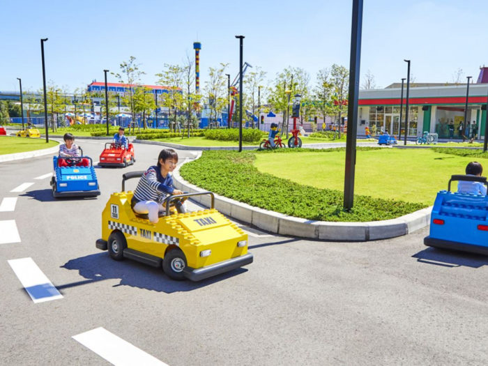 Happy children driving LEGOland cars, enjoying a playful and engaging experience in a colorful amusement park setting