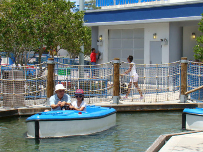 Two people driving a blue Lego boat, manufactured by SBI Sweden, at a Legoland attraction.