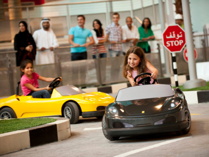 Happy girls driving cars at Ferrari World in Dubai, enjoying a fun and exhilarating experience in a vibrant amusement park setting