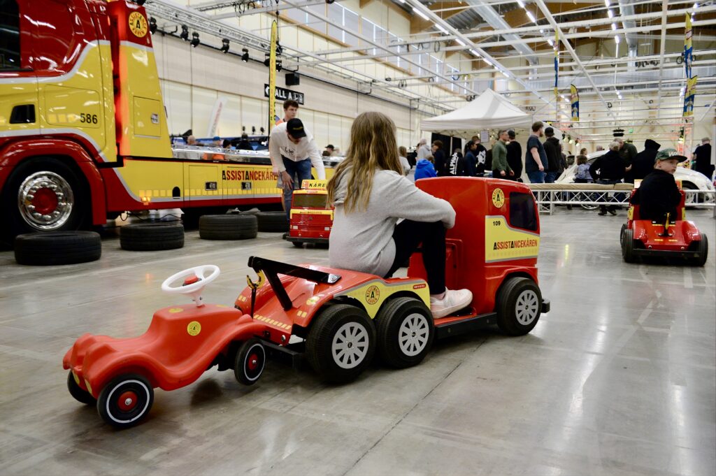 a girl driving a mini tow truck and towing a bobby car behind