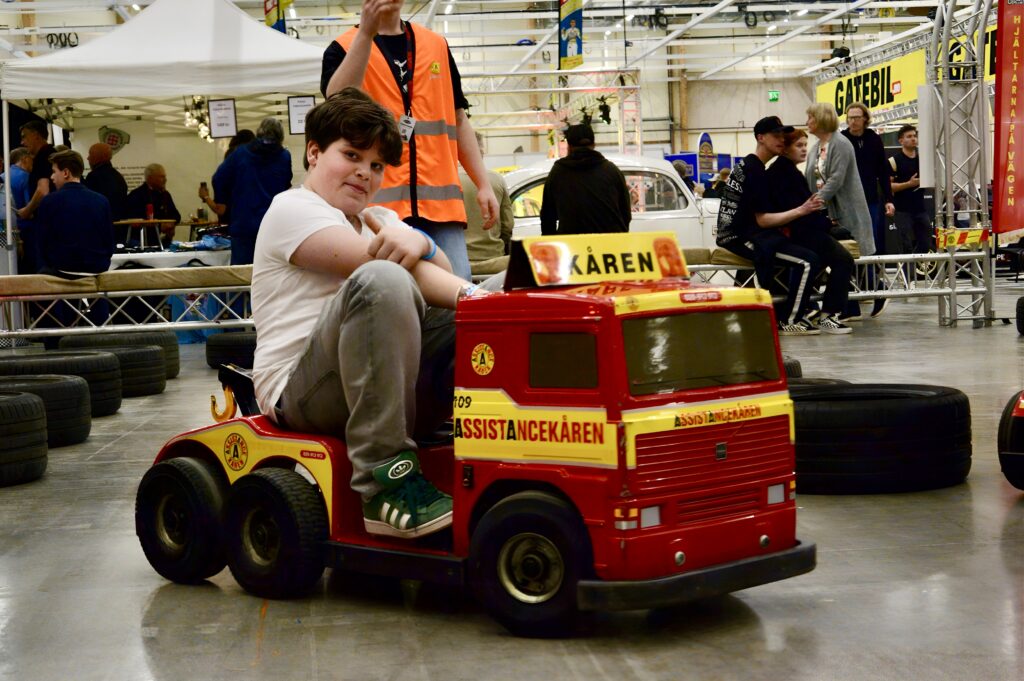 a boy on a mini tow truck doing a thumbs up sign